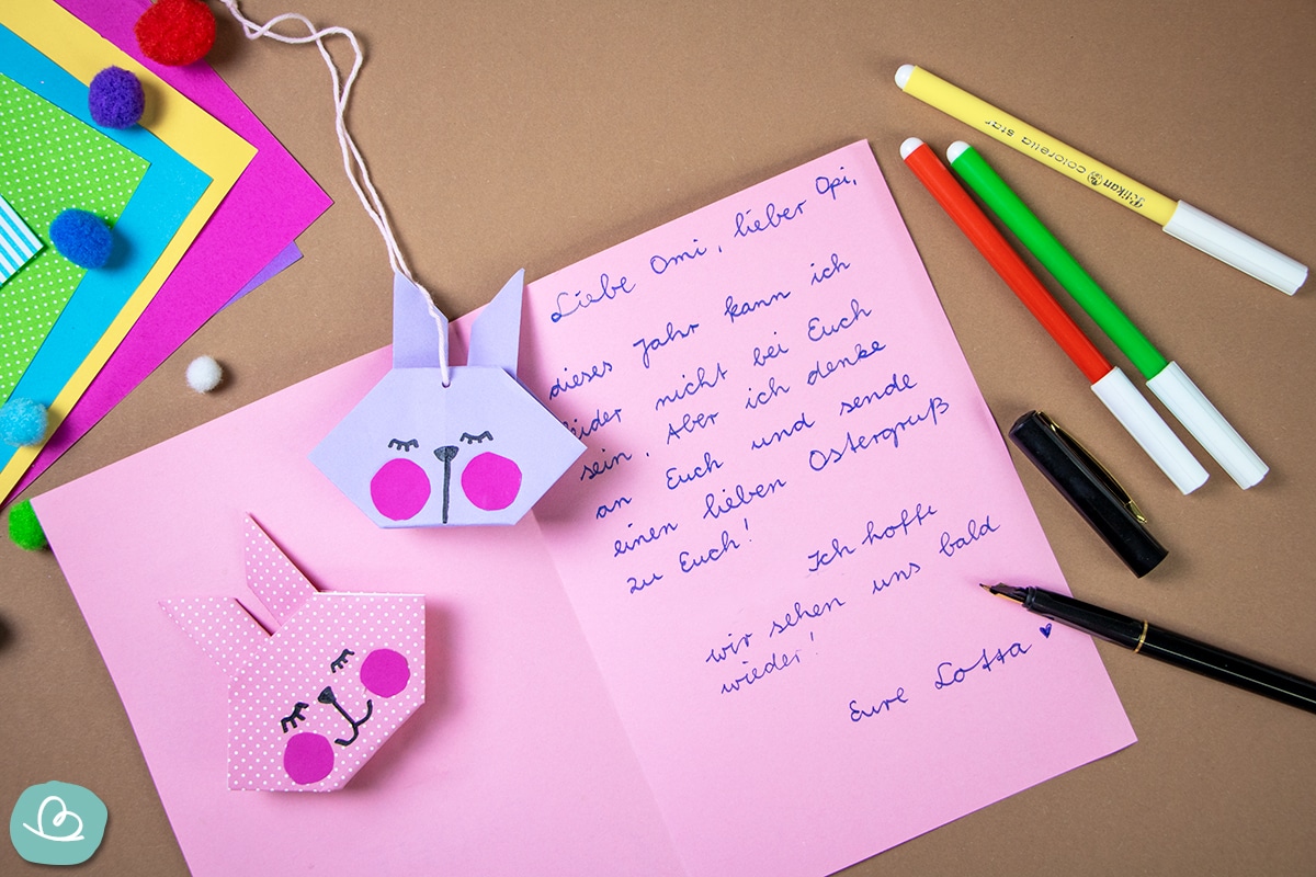 Origami Hasen auf einem Brief liegend für die Großeltern. Daneben liegt buntes Bastelmaterial.