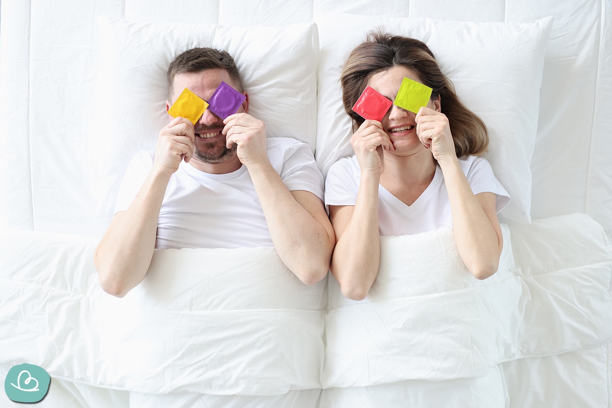 Verliebtes Paar im Bett liegend mit bunten Kondomen.