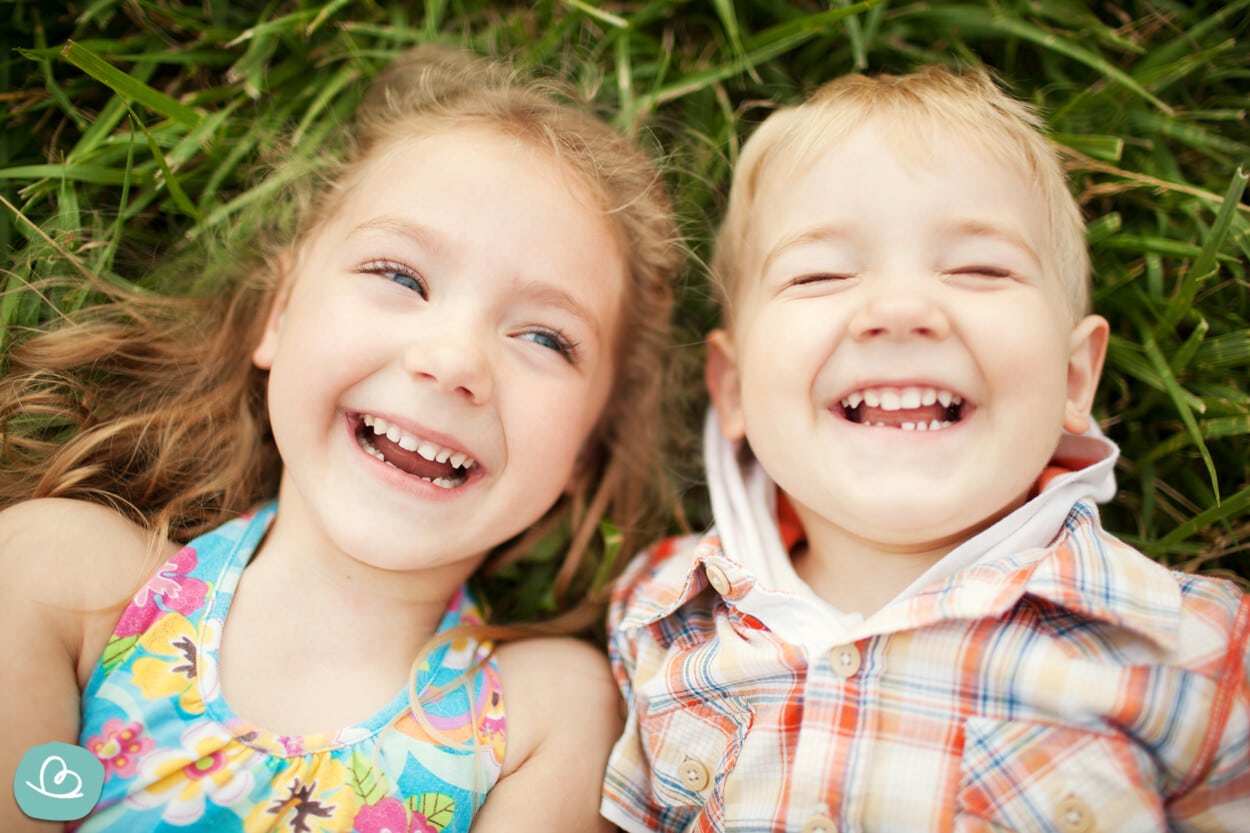 Zwei Kindner liegen im Gras und lachen zusammen.