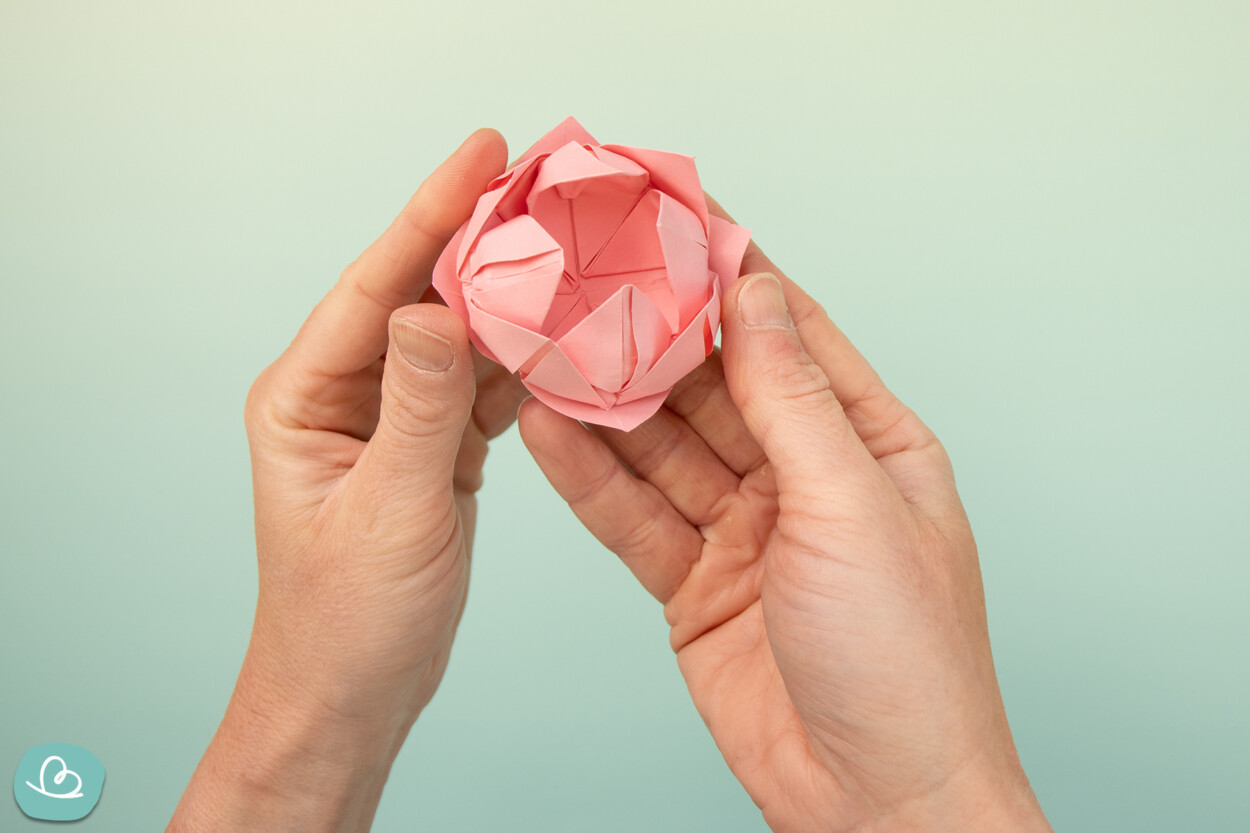 Lotusblüte aus Papier in den Händen haltend