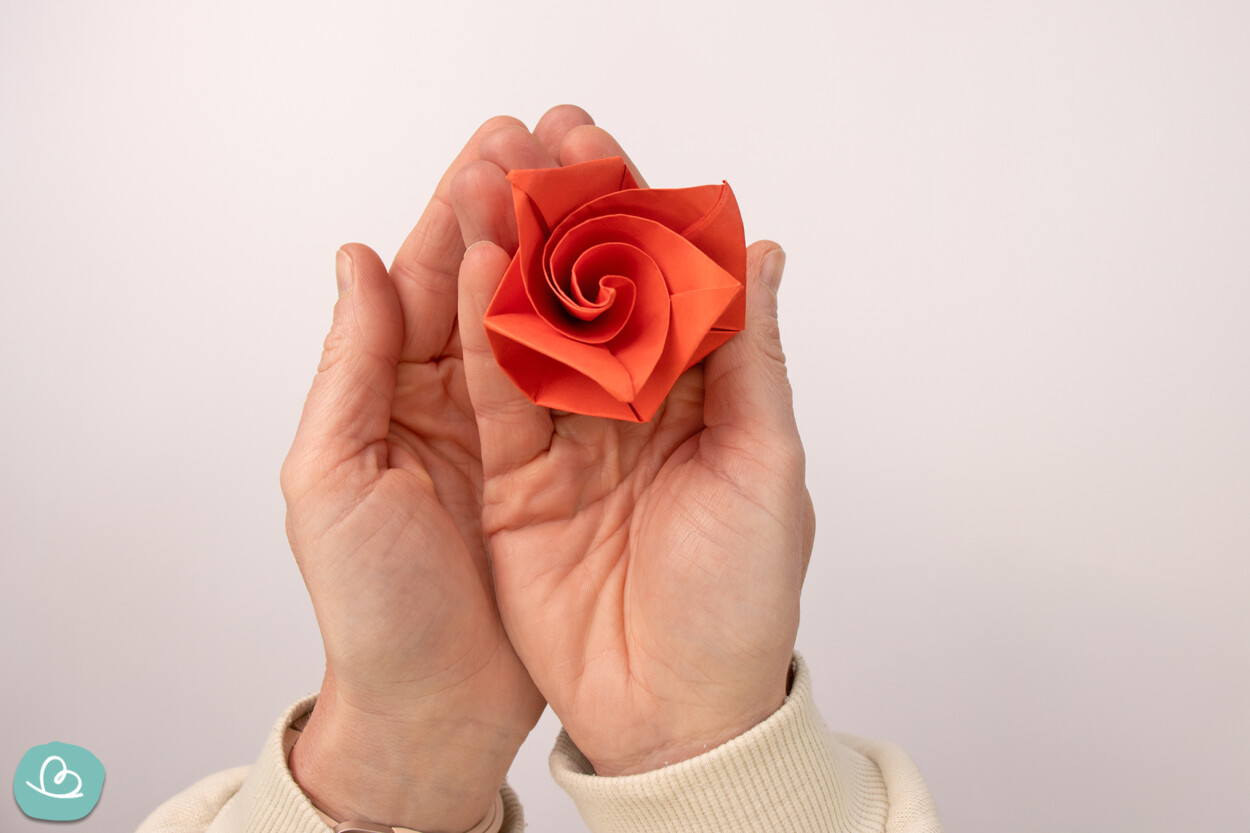 Gefaltete rote Origami Rose in den Händen haltend