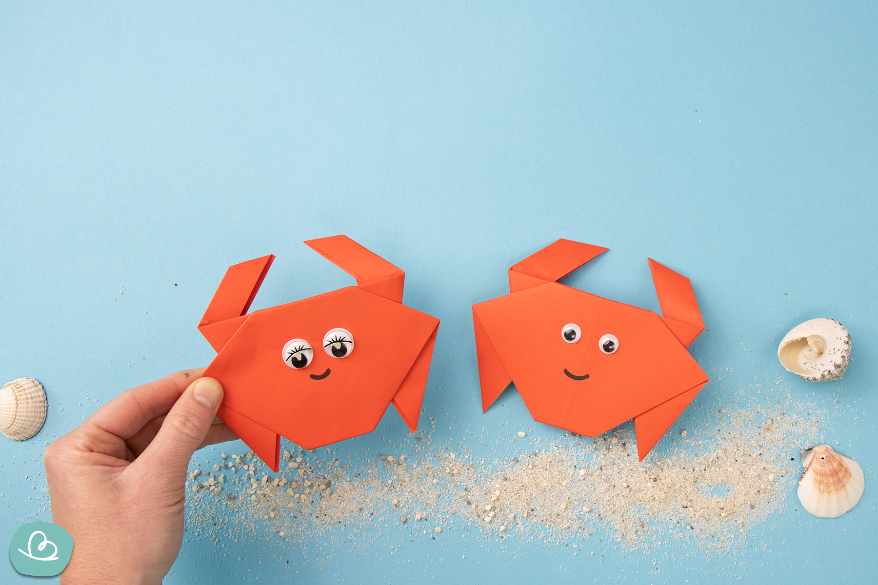 Der gefaltete Origami Krebs liegt als Dekoration auf blauem Papier, das wie ein Meer gestaltet ist.